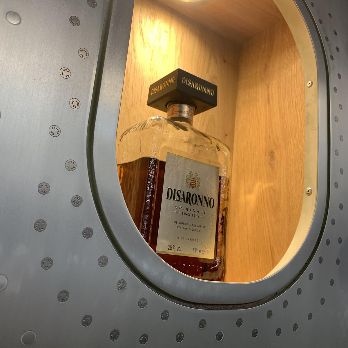 Brushed aircraft window section wall bar holding a Disaronno bottle.