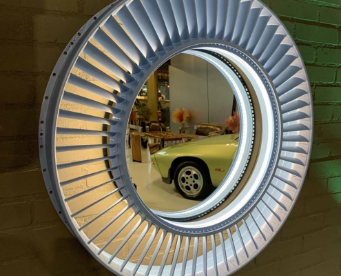 Mirror made from a Pratt & Whitney jet engine stator hanging on a brick wall in Kaeve, reflecting a Porsche car.